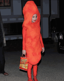 a woman in an orange costume holds a bag of cheetos