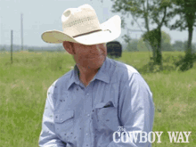 a man wearing a cowboy hat and a blue shirt is sitting in a field with the cowboy way written on the bottom