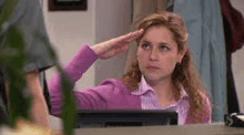 a woman is saluting while sitting at a desk in front of a computer monitor .