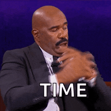 a man in a suit and tie is sitting in front of a purple background and says `` time '' .