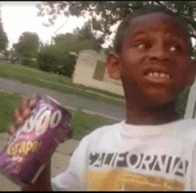 a young boy in a california shirt is holding a can of grape soda .