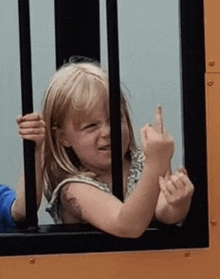 a little girl is behind bars and giving the middle finger