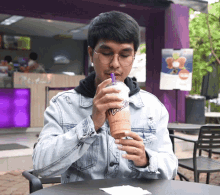 a man in a denim jacket is drinking a smoothie from a cup that says ' ice cream ' on it