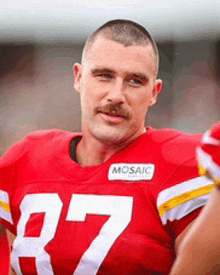 a man with a mustache wearing a red jersey with the number 27 on it