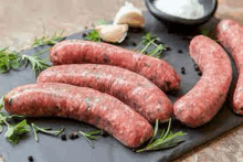 a bunch of sausages are sitting on top of a cutting board with herbs .