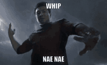 a man is standing in the dark with his arms outstretched and the words whip nae nae written on his chest .