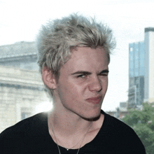 a young man with blonde hair is wearing a black shirt and making a funny face .