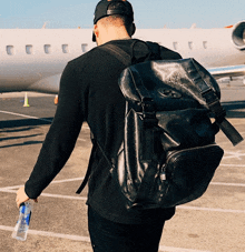 a man carrying a large black backpack with the letter a on it walks towards an airplane