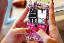 a woman is holding a pink phone with a rhinestone case on it .