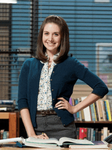 a woman wearing a blue cardigan stands in front of a bookshelf