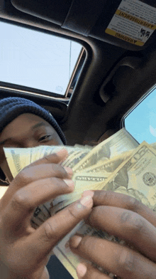 a man in a car holds a stack of 20 dollar bills in front of his face