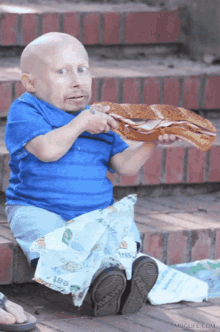 a little boy is sitting on a set of stairs eating a sandwich with a bag that says free on it