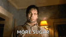 a man in overalls is standing in a dark room with the words `` more sugar '' written on his chest .