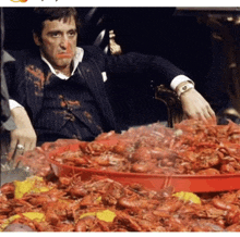 a man in a suit sits at a table with a tray of crawfish