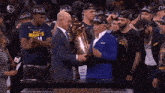 a man in a suit holds a trophy in front of a group of basketball players wearing hats that say champions