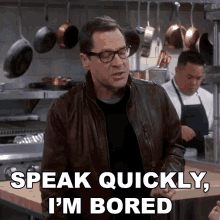 a man wearing glasses and a leather jacket says " speak quickly i 'm bored "