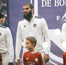 a man with a beard wearing a white adidas jacket