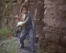 a group of men are standing in front of a brick wall and one of them is pointing a gun