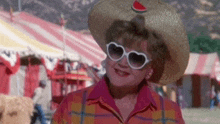 a woman wearing a hat and heart shaped sunglasses is standing in front of a circus tent .