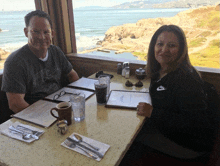 a man and a woman are sitting at a table with a view of the ocean