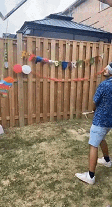 a man is standing in front of a wooden fence with balloons and a banner that says ' happy birthday '