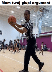 a referee is holding a basketball on a basketball court in front of a group of people playing basketball .