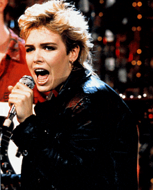 a woman singing into a microphone while wearing a leather jacket