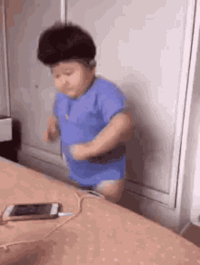 a baby is standing on a bed next to a cell phone .