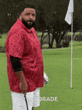 a man in a red shirt and white shorts is standing on a golf course holding a golf club and a gatorade bottle