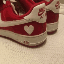 a pair of red and white nike air force 1 sneakers with a heart embroidered on the back .