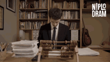 a man in a suit and tie is using an abacus in front of a bookshelf with the words nipio dram on the bottom