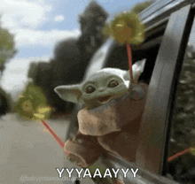 a baby yoda is sticking its head out of a car window and holding a lollipop .