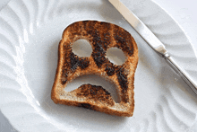 a slice of toast with a sad face drawn on it is on a plate with a knife