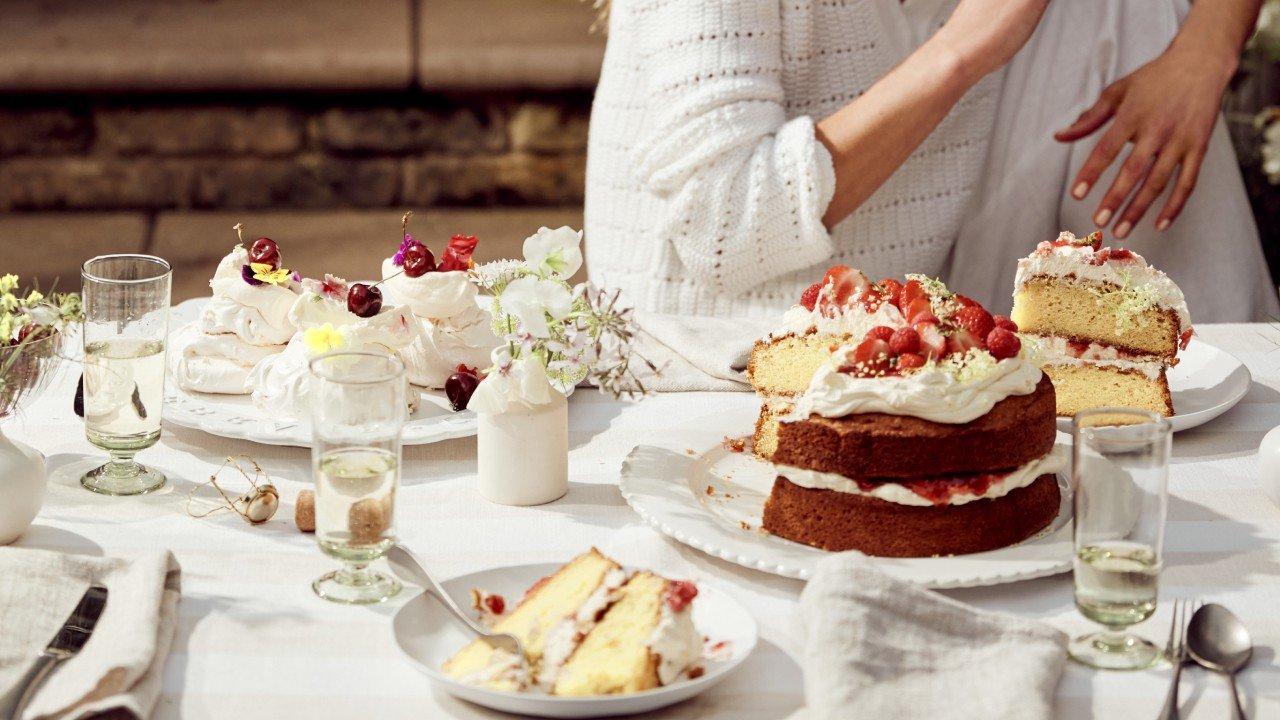 a woman holding a baby while standing in front of a table with cakes