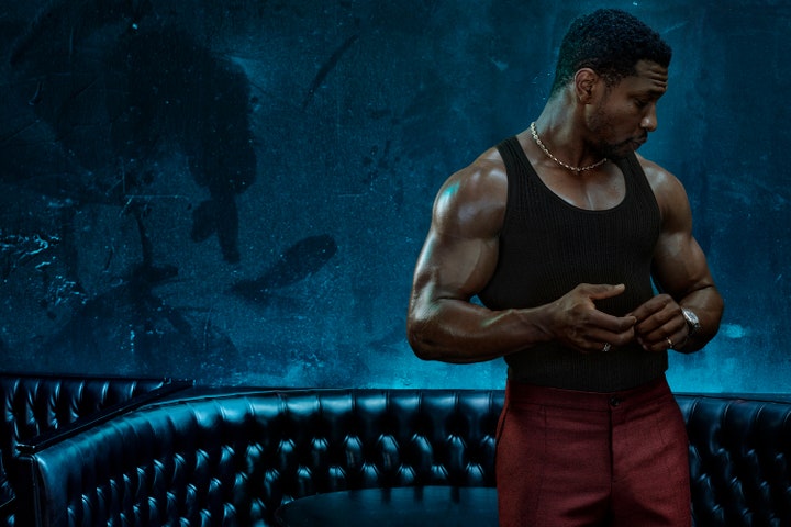 Jonathan Majors standing in a bar wearing a Tom Ford tank top and Dolce  Gabbana pants.