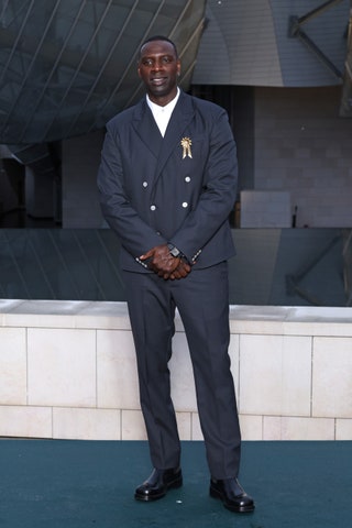 Image may contain Omar Sy Person Standing Adult Wristwatch Clothing Footwear Shoe and Coat