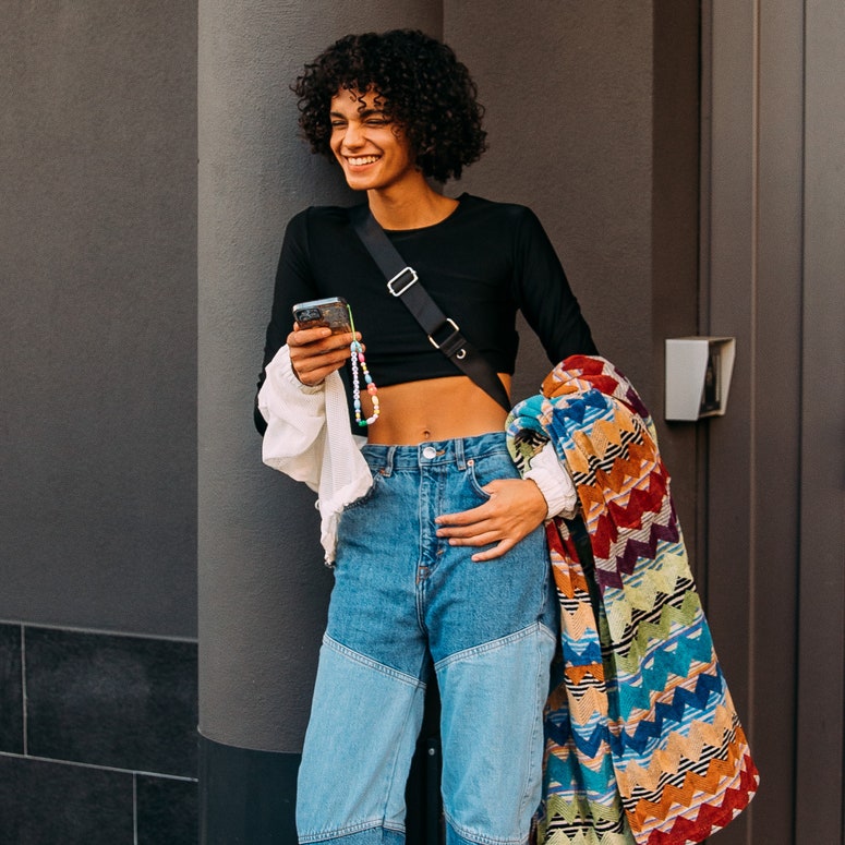 Mujer con crop top negro con mangas largas y pantalones jeans de patchwork y abrigo estilo Missoni 