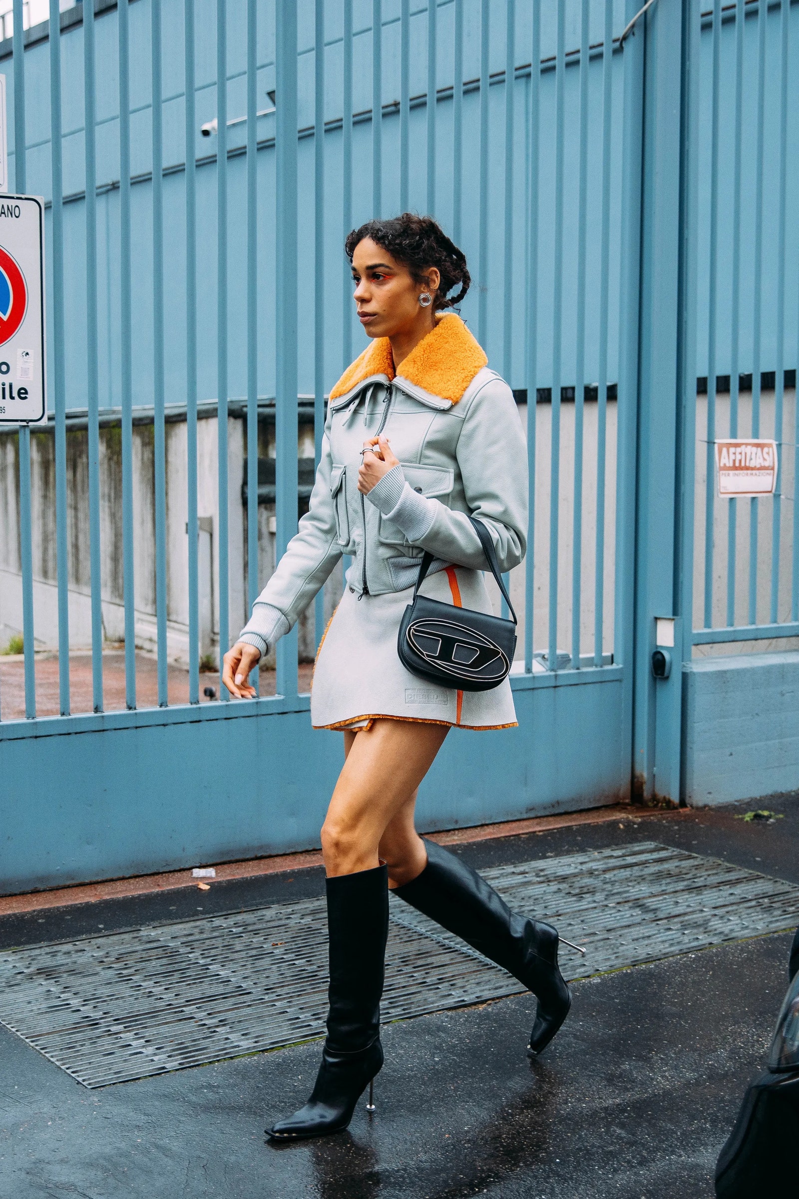 mujer con mini falda blanca chaqueta azul botas altas negras y bolsa diesel 1dr