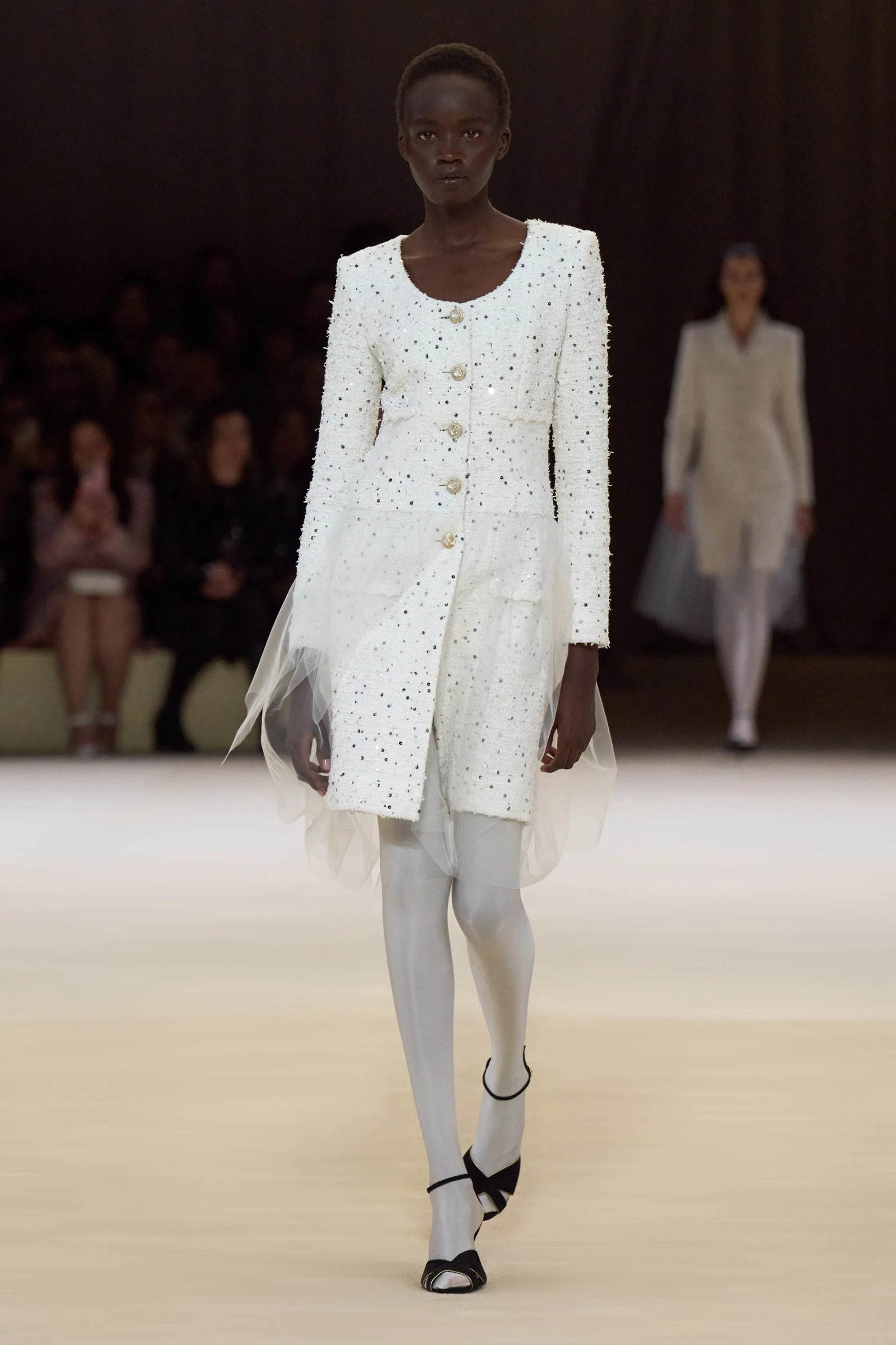 Modelo luce un vestido blanco con medias blancas y zapatos de tacón en Chanel PrimaveraVerano 2024