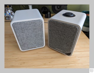 Two grey square shaped speakers with grey fabric covers on the front of each