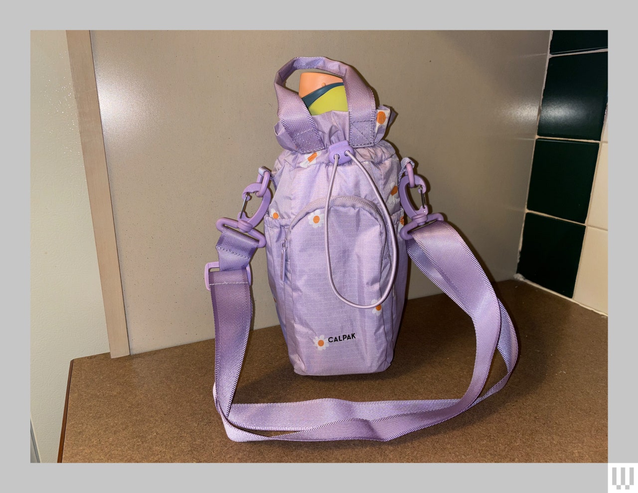 Purple pouch with long strap holding a reusable water bottle inside, sitting on a dark counter