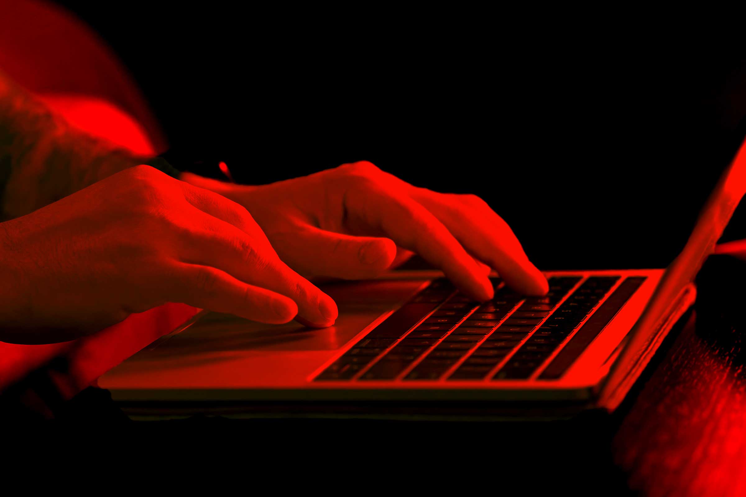 Closeup of hands typing on a laptop keyboard under red lighting