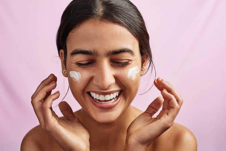 Studio shot of a beautiful young woman applying moisturizer to her face