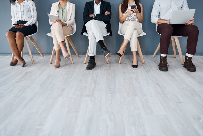 Closeup shot of a group of unrecognisable businesspeople using digital devices while sitting in line against a grey background awaiting a job interview