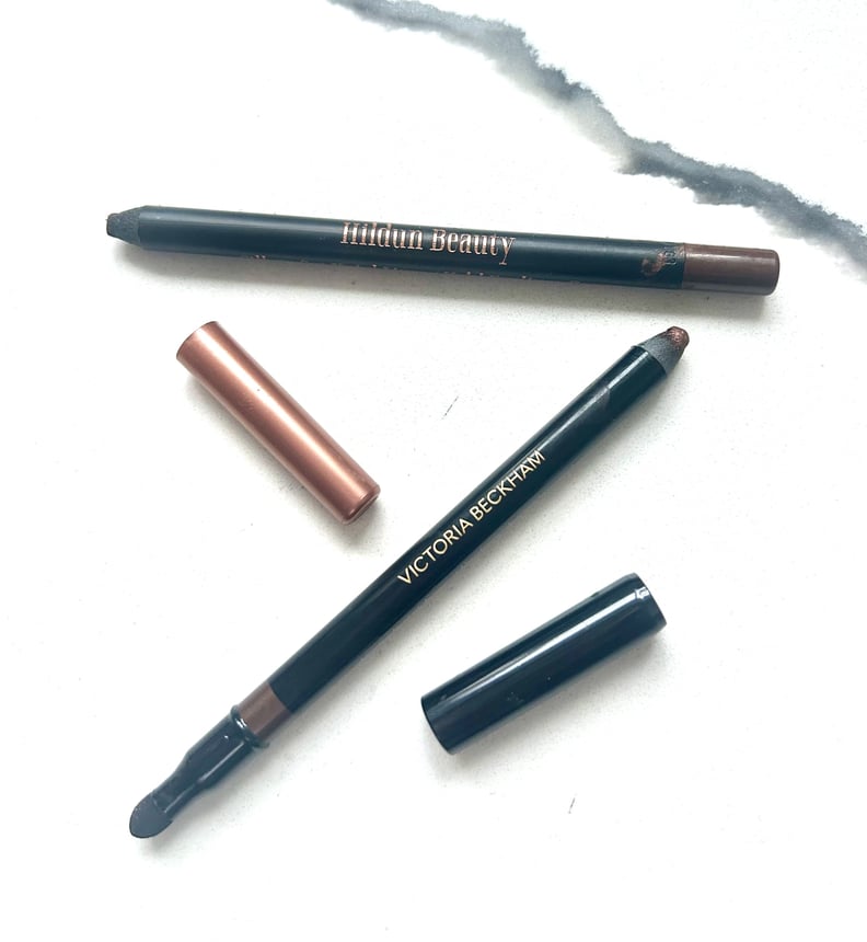 Hildun and Victoria Beckham Eyeliner pencils with lids off on a marble surface