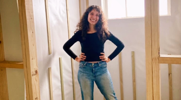 A woman smiles in interior of building that is under construction.