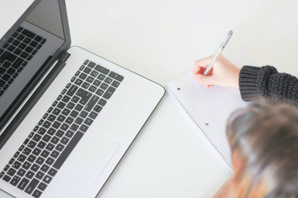 A student writes in a notebook next to an open laptop.