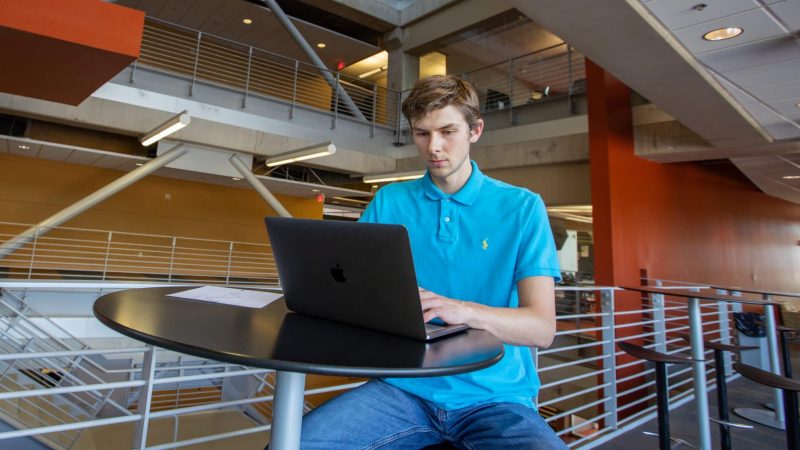 Student sits at table with laptop.