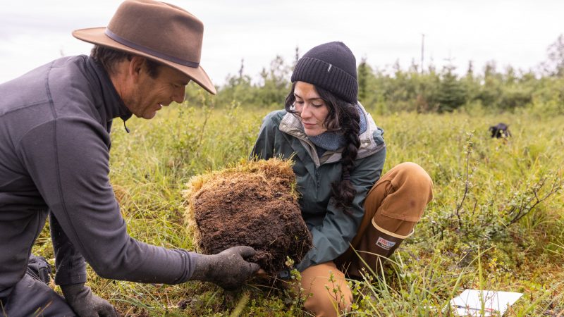 Graduate student and professor observe soil in a field.