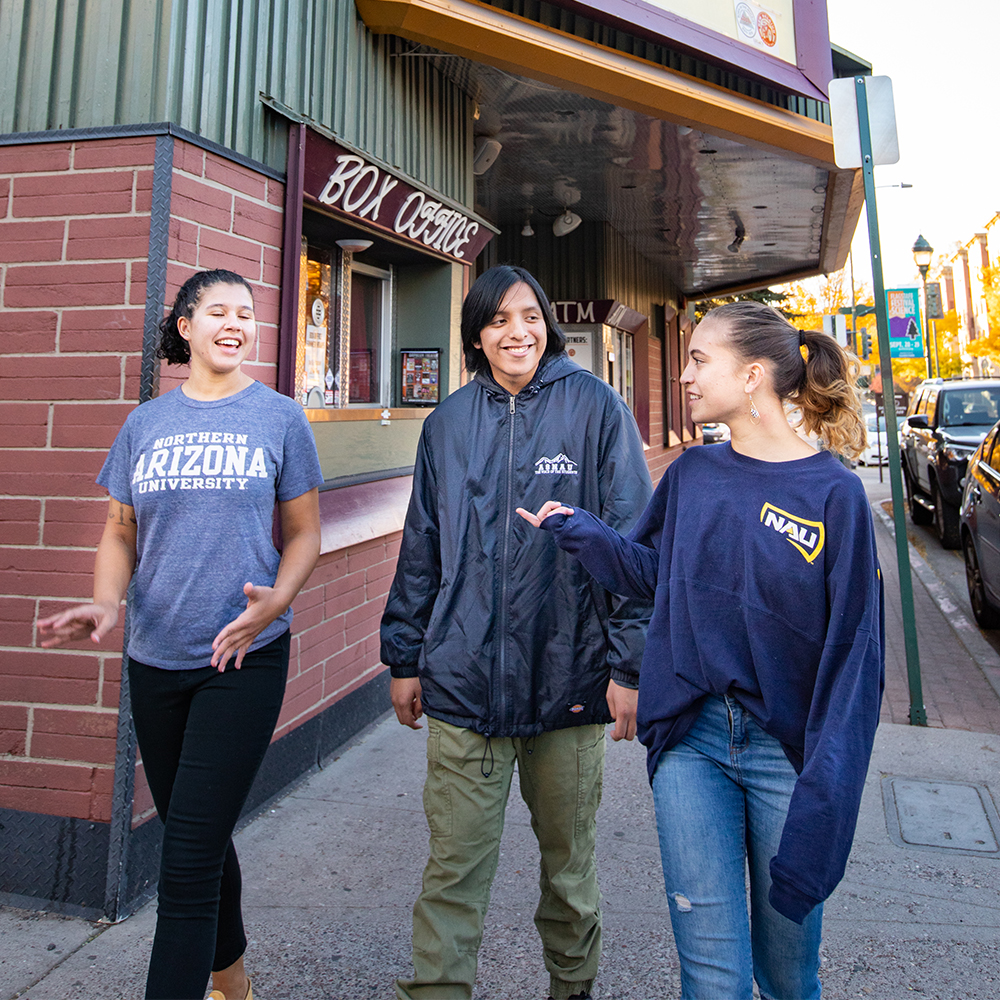 NAU students wearing shirts with school logo walking together on a sidewalk and talking